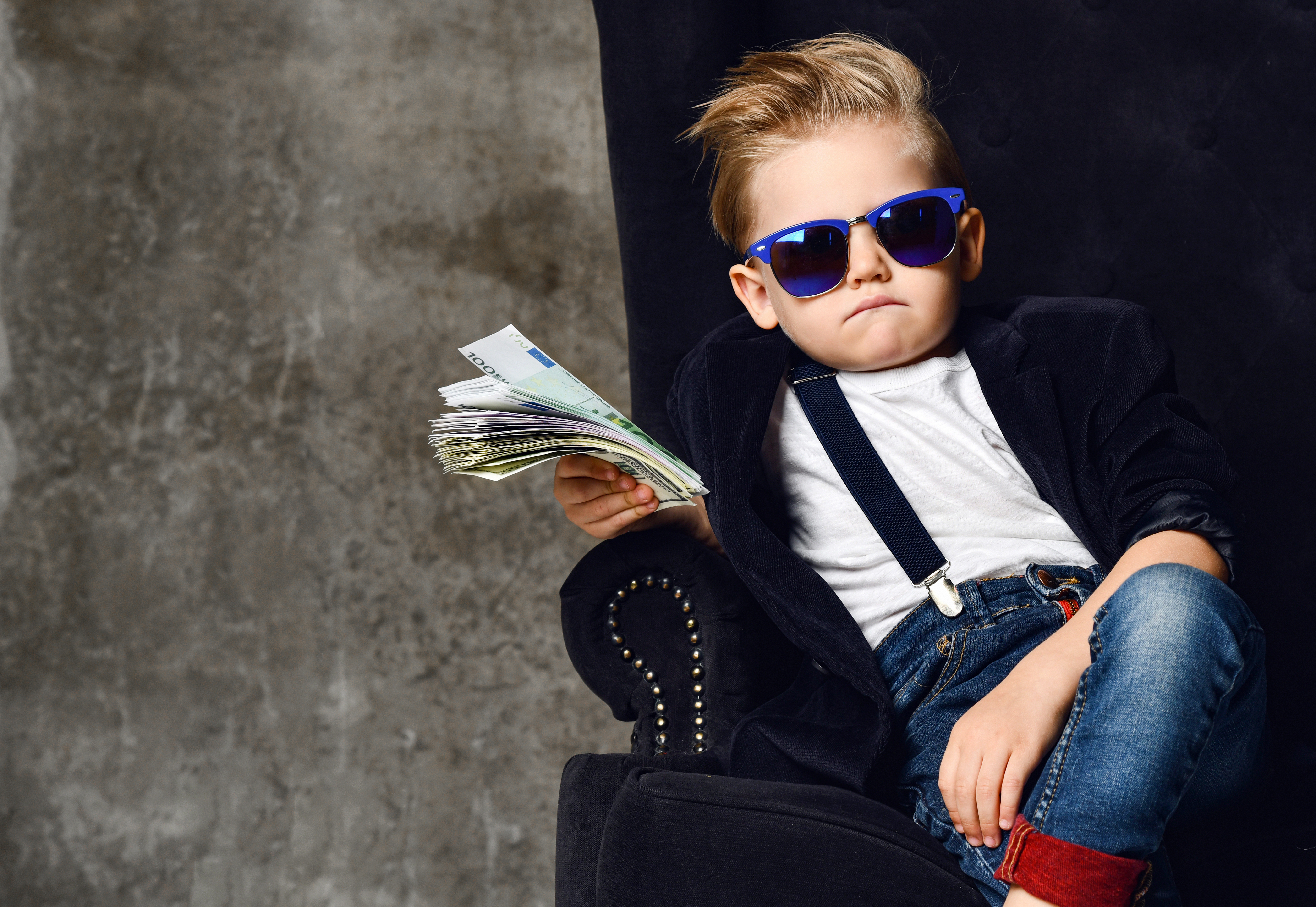 Boy in sunglasses sitting in a chair and holding a stack of banknotes